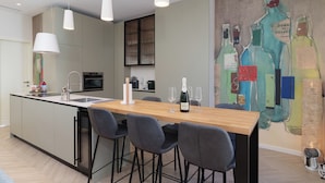 Una cocina moderna con una isla central, taburetes de bar, iluminación colgante y un mural de botellas de vino en la pared.