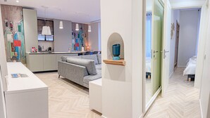 Habitación de hotel moderna con sofá, una mesita, espacio de cocina y baño a la vista a través de una puerta abierta.
