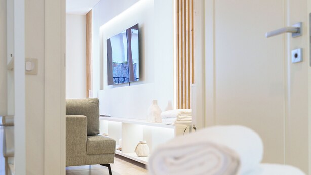 Habitación de hotel con cama, una silla, televisor montado en la pared y baño visible a través de una puerta abierta.