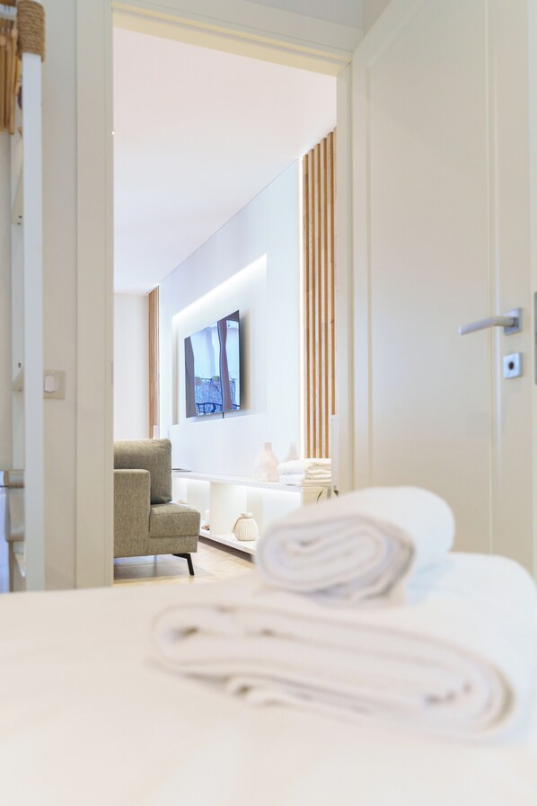 Ein Hotelzimmer mit einem Bett, einem Sessel, einem an der Wand befestigten Fernseher und einem durch eine offene Tür einsehbaren Badezimmer.
