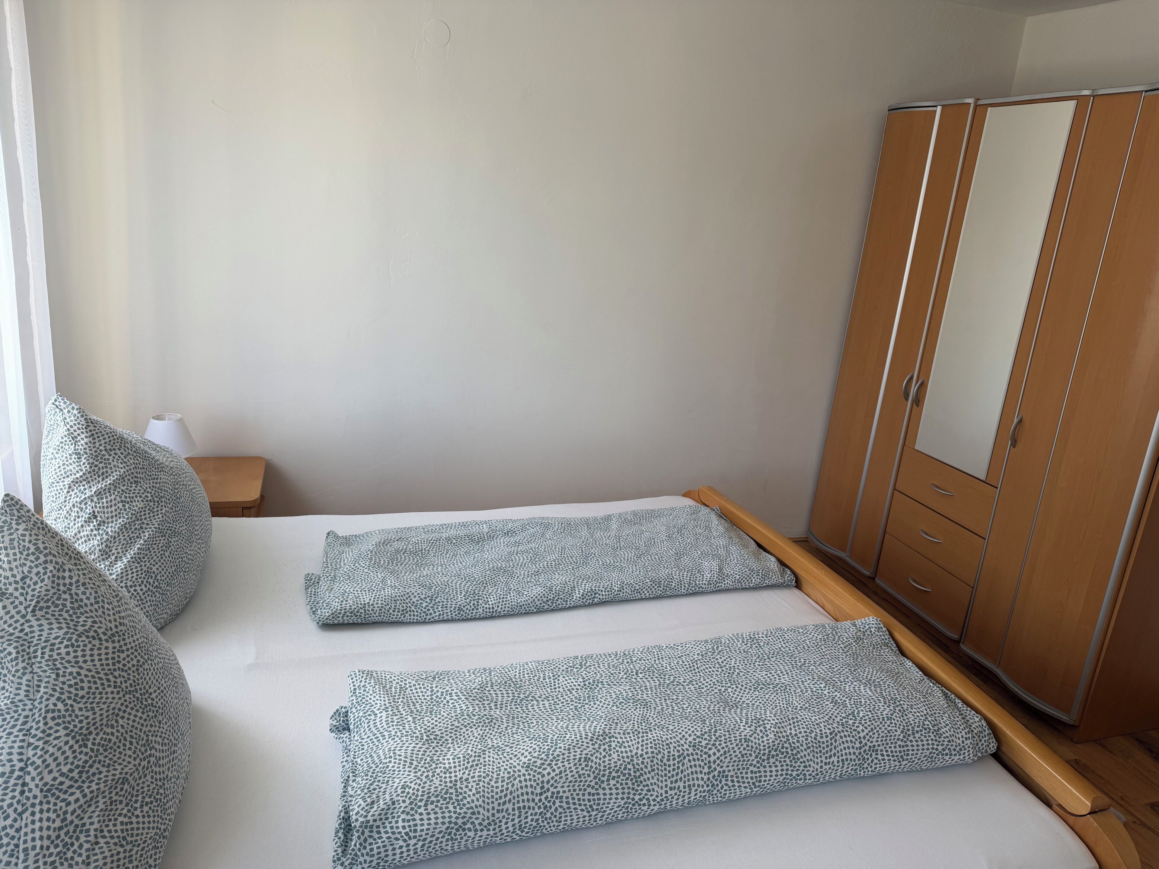 Une chambre à coucher avec un lit, deux oreillers, une armoire en bois et une petite table avec une lampe.