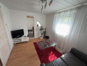 Una sala de estar con televisor, una mesa de centro de vidrio, alfombra roja, sofá y una escalera que lleva a otra habitación.