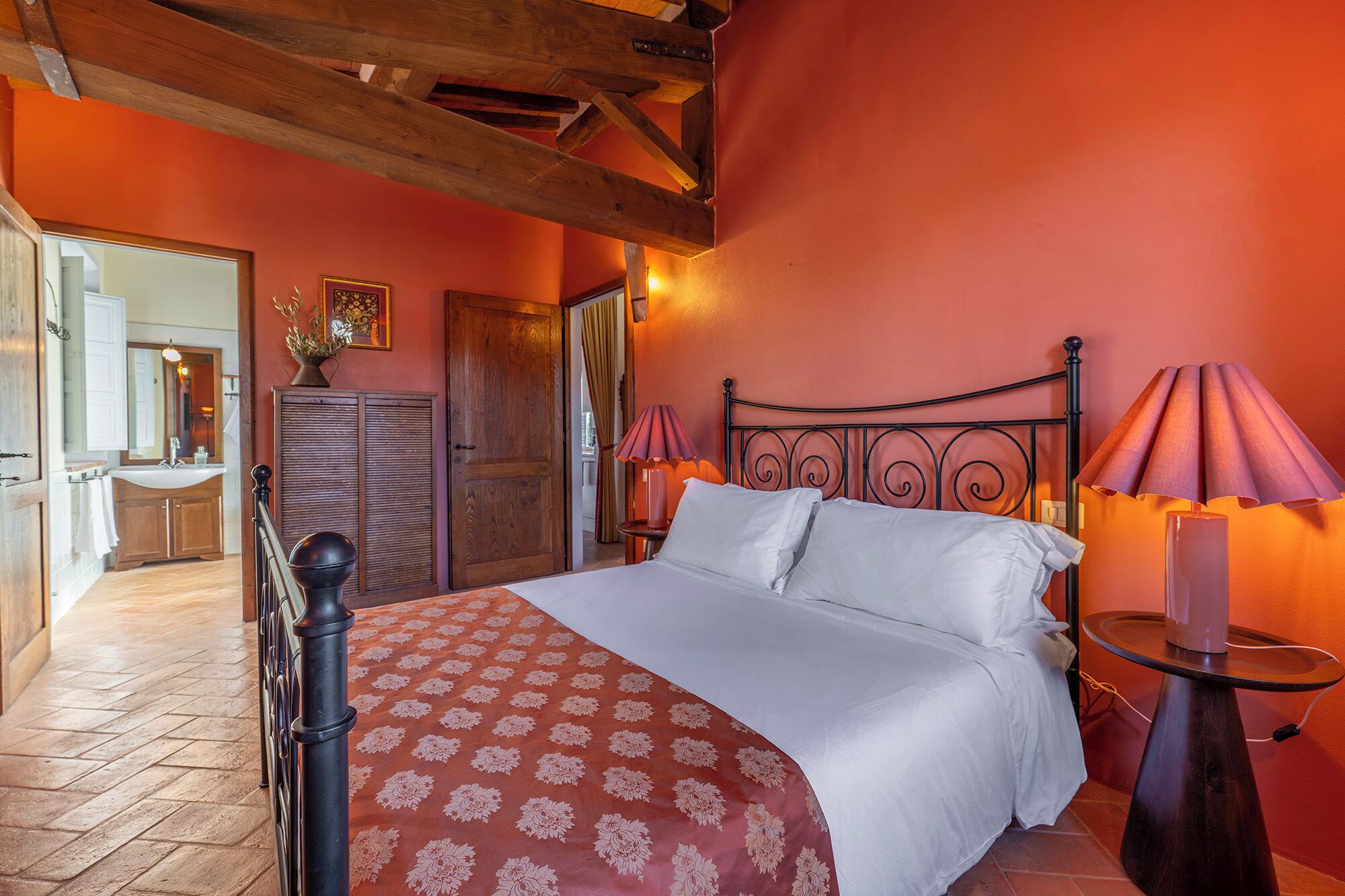 A bedroom with a bed, two bedside lamps, a wooden headboard, and a door leading to a bathroom.