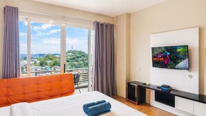 A hotel room with a bed, a TV, a desk, and a view of a cityscape.