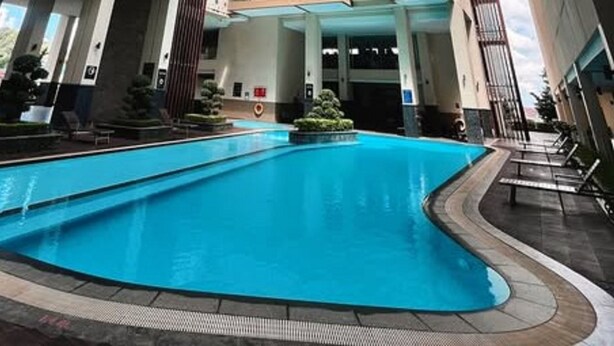 A swimming pool with a curved edge, surrounded by a tiled deck and a few lounge chairs.