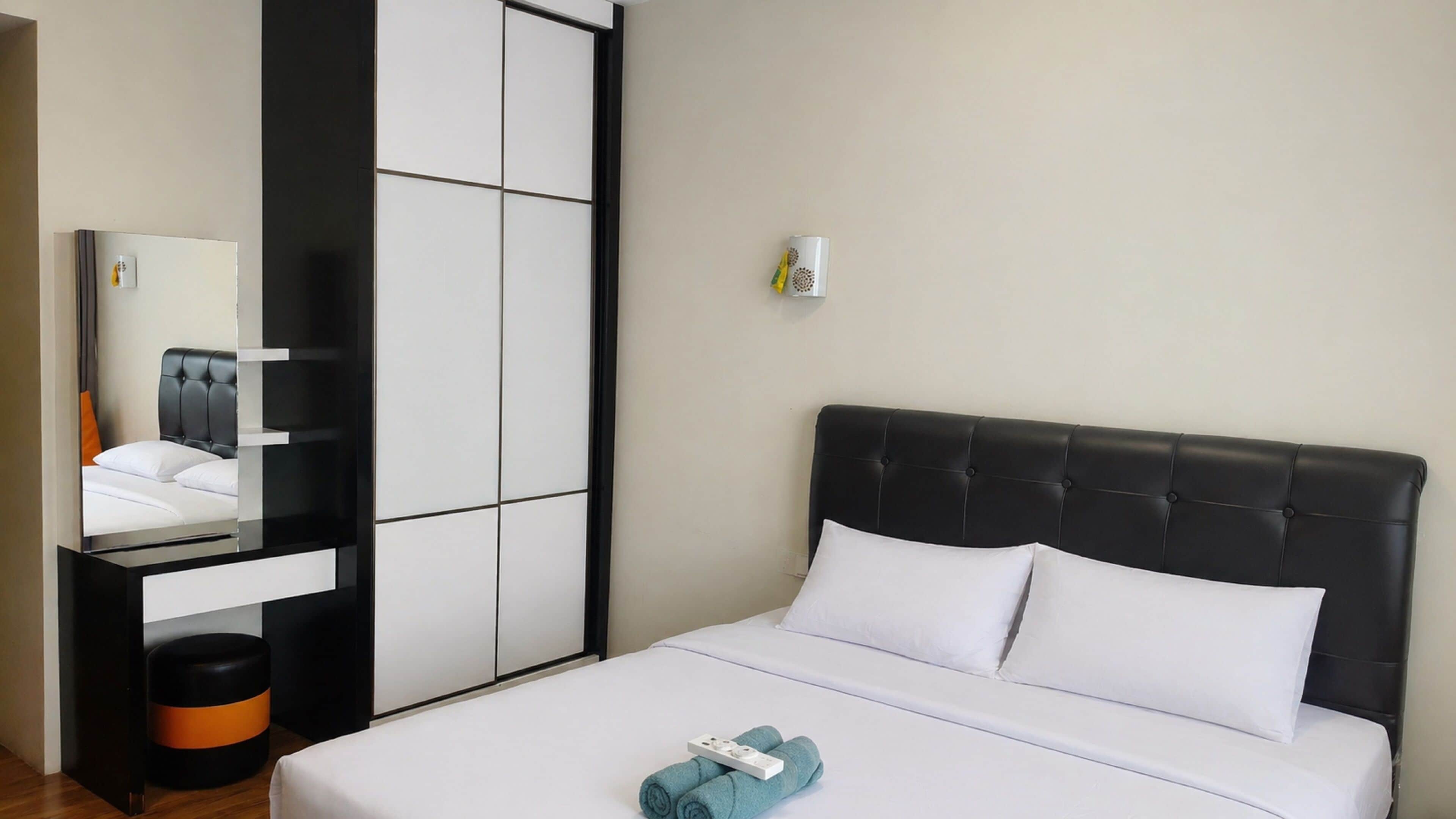 A hotel room with a bed, a wardrobe, a mirror, and a small table.