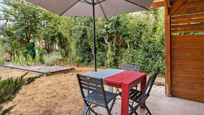 Eine Terrasse mit Tisch und Stühlen unter einem großen Sonnenschirm, umgeben von einem Garten mit verschiedenen Pflanzen und einem Holzzaun.