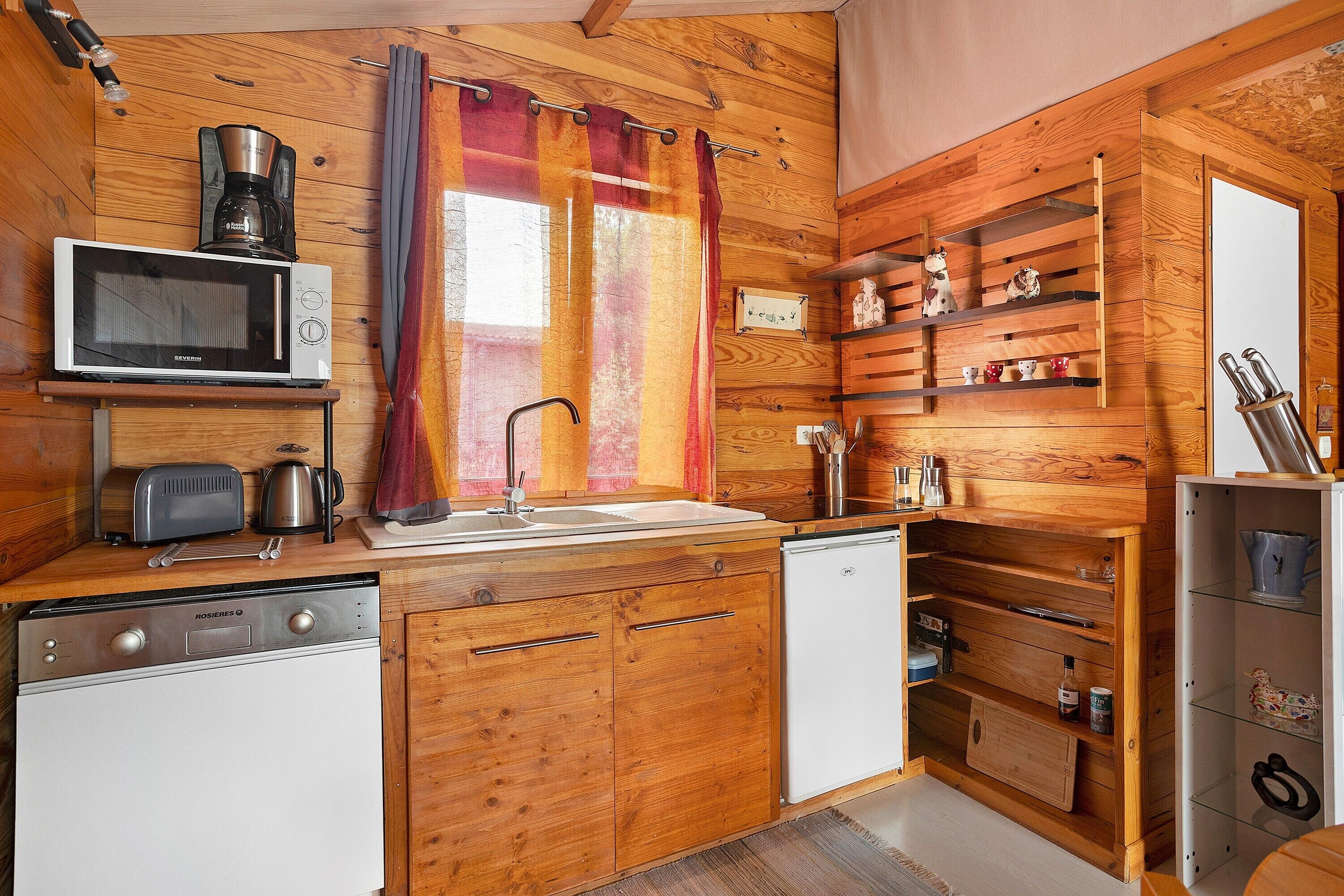 Eine kleine Küche mit Holzschränken, einer Mikrowelle, einem Toaster, einer Spüle und einem Kühlschrank.