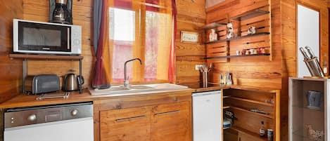 A compact kitchen with wooden cabinetry, a microwave, a toaster, a sink, and a refrigerator.
