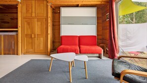 Ein Zimmer mit Holzvertäfelung, einem roten Sofa, einem weißen Tisch und einem Fenster mit gelbem Vorhang.