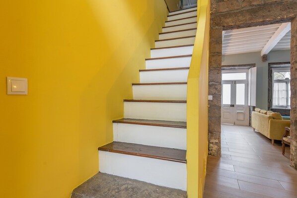 Eine Treppe mit weißen Stufen und einer gelben Wand, die zu einem Raum mit Holzboden und einem gelben Sofa führt.