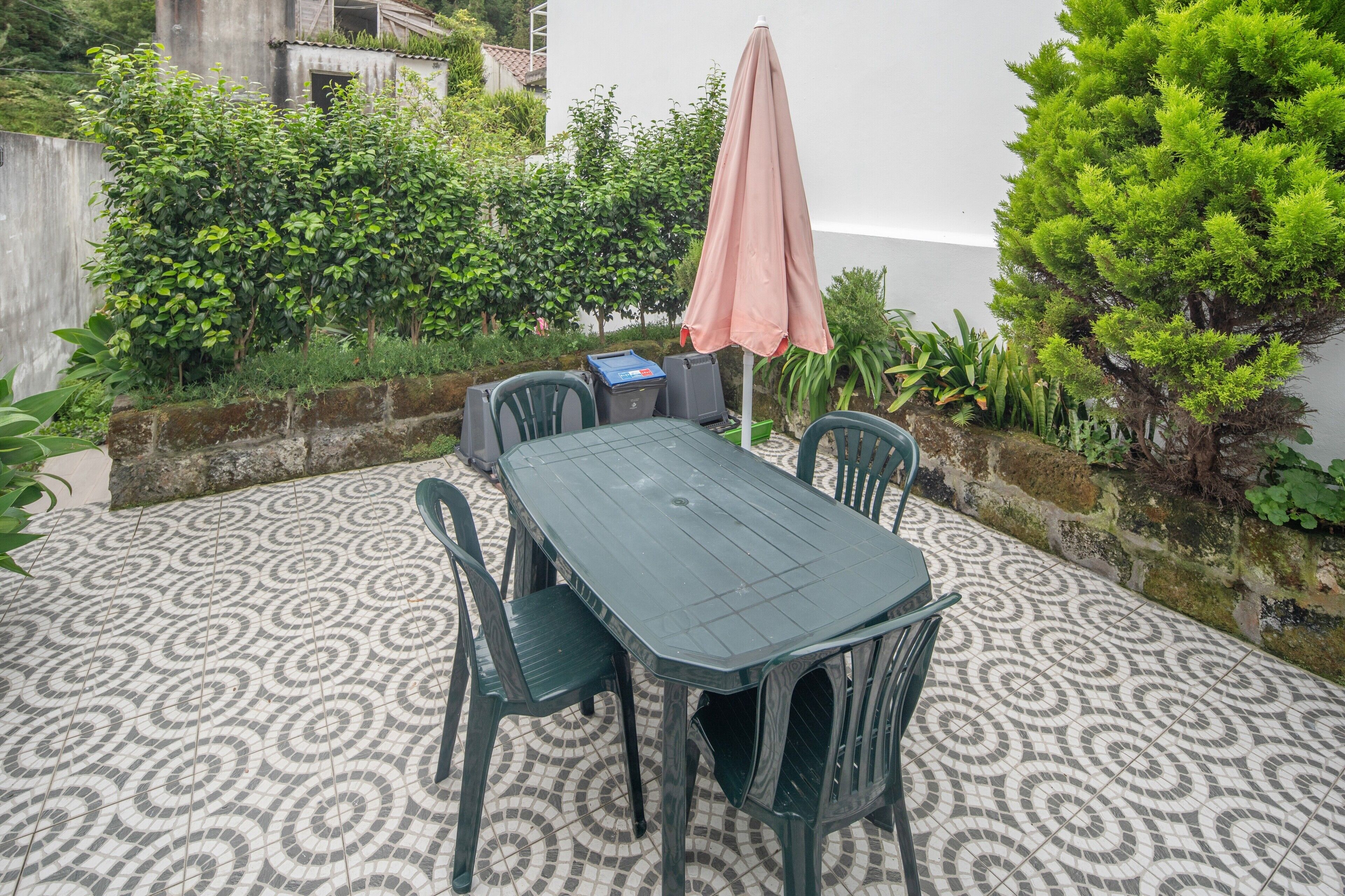 Eine Terrasse mit Tisch und Stühlen, umgeben von Grünpflanzen und einem gemusterten Boden.
