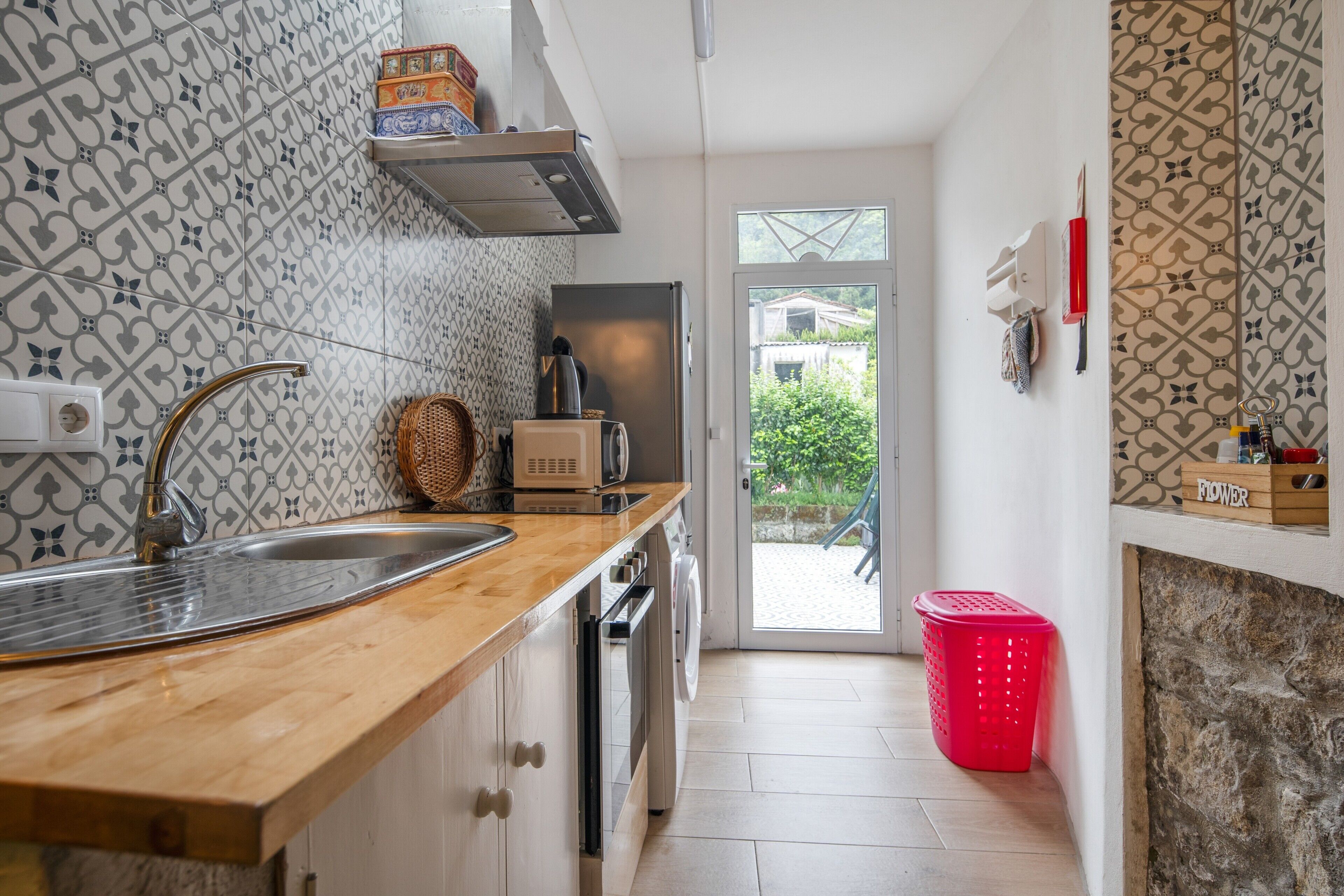 Een keuken met een houten aanrecht, een roestvrijstalen spoelbak en een rode wasmand.