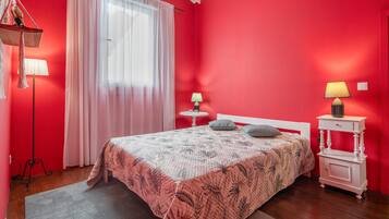 Ein Schlafzimmer mit einem Bett, zwei Nachttischen, einem Fenster mit Vorhängen und einer roten Wand.