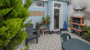 Un patio con suelo estampado, una mesa, sillas, un taburete pequeño, una planta en maceta y un horno de ladrillo.