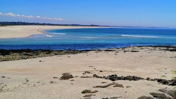 En strand med kristallklart blått vatten, en sandstrand och en avlägsen horisont.