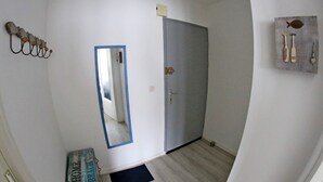 En hall med en spegel, en dörr, en väggmonterad lampa och en liten matta.