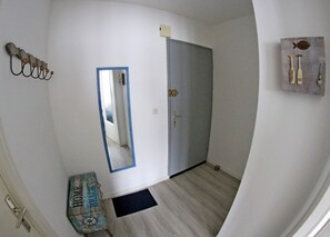 A hallway with a mirror, a door, a wall-mounted light fixture, and a small rug. - Charming family studio by the white sea at Le Letty in Bénodet (Bénodet)