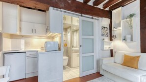 Une cuisine compacte avec des meubles blancs, un plan de travail blanc et une porte coulissante donnant sur une salle de bain.