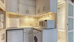 Une cuisine compacte équipée d’un lave-linge, d’un four à micro-ondes et d’un petit réfrigérateur.