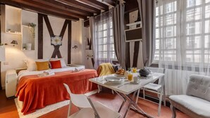 Une chambre d’hôtel avec un lit, une table à manger où le petit-déjeuner est servi, une chaise, un canapé et une grande fenêtre avec des rideaux.