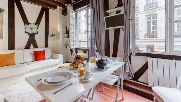 Un coin repas avec une table mise pour le petit-déjeuner, un canapé avec des coussins et une fenêtre avec des rideaux.