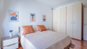 Een slaapkamer met een bed, nachtkastje, kledingkast en abstracte wanddecoratie.