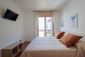 A bedroom with a bed, a TV mounted on the wall, and a window with curtains.