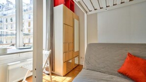 Un dormitorio con cama, armario, ventana y vistas a edificios.