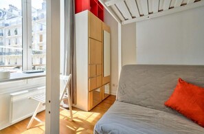Ein Schlafzimmer mit Bett, Kleiderschrank, Fenster und Blick auf Gebäude.