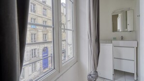 Une pièce avec une fenêtre, un lavabo blanc et un miroir.
