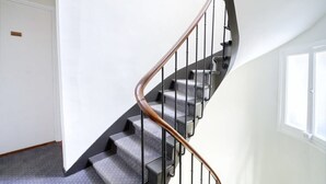 Un escalier doté d’une main courante en bois et de balustrades en métal, menant à une pièce avec une porte blanche et une fenêtre.