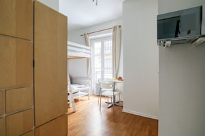 Ein Zimmer mit Etagenbett, Esstisch mit Stühlen, Wandfernseher und einem Fenster mit Vorhängen.