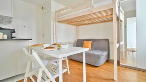 Ein kompakter Wohnbereich mit Küchenzeile, einem Esstisch mit Stühlen, einem grauen Sofa und einer Holzbalkendecke.