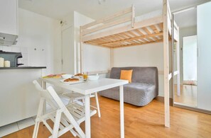 Ein kompakter Wohnbereich mit Küchenzeile, einem Esstisch mit Stühlen, einem grauen Sofa und einer Holzbalkendecke.