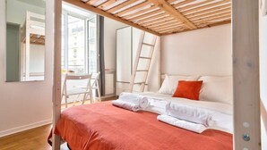 Un dormitorio con techo de madera, cama con sábanas blancas, una manta roja y una silla blanca.