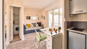 Un apartamento pequeño con kitchenette, zona de comedor, sofá con cojines, lavadora y ventana.
