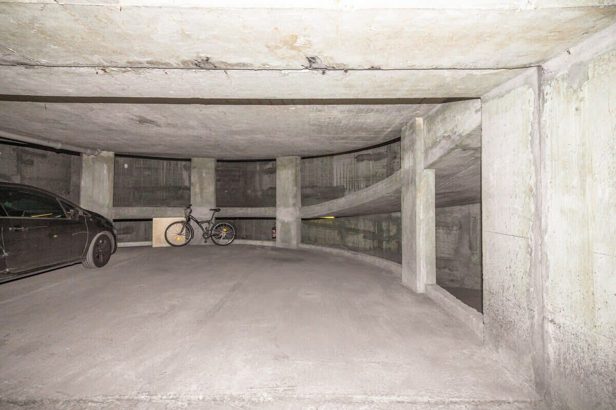An underground parking garage with concrete pillars, a car, and a bicycle.