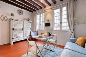 A room with a dining table, chairs, a sofa, a cabinet, and a window with curtains. - New & Authentic Studio - The Historical Le Marais (Paris)