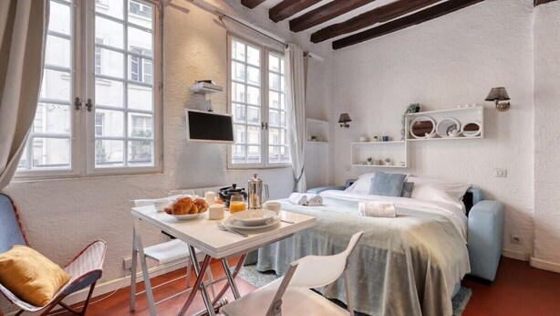 Una habitación de hotel compacta con una cama, una mesita con desayuno, una silla y un televisor.