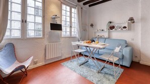 Una habitación con una mesa de comedor, sillas, un sofá azul, un televisor y un radiador.