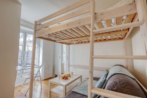 A bunk bed with a wooden frame, a small table with breakfast items, and a view of the city through large windows. - Studio Parfait - Coeur du 17em (Paris)