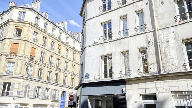 A multi-story building with balconies, a storefront, and a clear blue sky. - Welcoming Studio - Coeur du 17em - Bail moy durée (Paris)