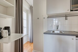 A kitchen with a sink, a window, and a door leading to a balcony. - Nicely designed Studio - Paris 17 - Mid Terms (Paris)