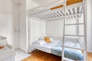 Ein Stockbett mit weißer Bettwäsche, ein Holzboden, ein weißer Schreibtisch mit Stuhl und eine weiße Tür.