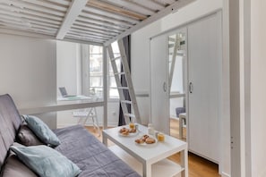 Ein modernes Zimmer mit einem grauen Sofa, einem weißen Tisch mit Frühstück, einer Hockerleiter und einer Schiebet ür.