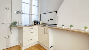 A modern kitchen with white cabinets, a wooden countertop, a window, a sink, and a small plant on the counter. - New, Large and Cosy Studio - Le Marais - Mid Terms (Paris)