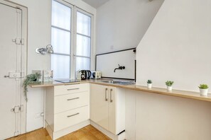 A modern kitchen with white cabinets, a wooden countertop, a window, a sink, and a small plant on the counter. - New, Large and Cosy Studio - Le Marais - Mid Terms (Paris)