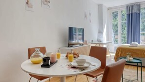 A dining area with a round table, chairs, breakfast items, and a television. - New, Large and Cosy Studio - Le Marais - Mid Terms (Paris)