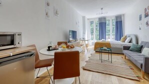 A modern, well-lit room with a dining table, chairs, a sofa, a bed, a TV, and a microwave. - New, Large and Cosy Studio - Le Marais - Mid Terms (Paris)